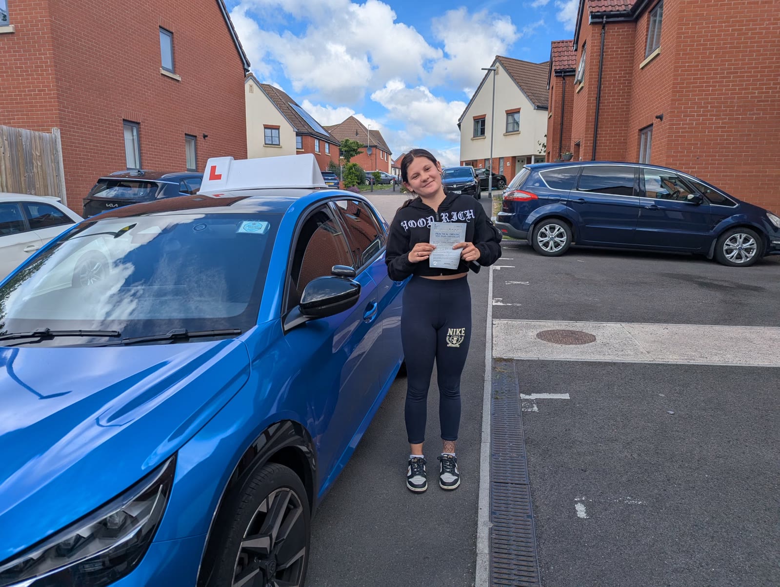 A learner celebrates passing their driving test beside the blue tuition car