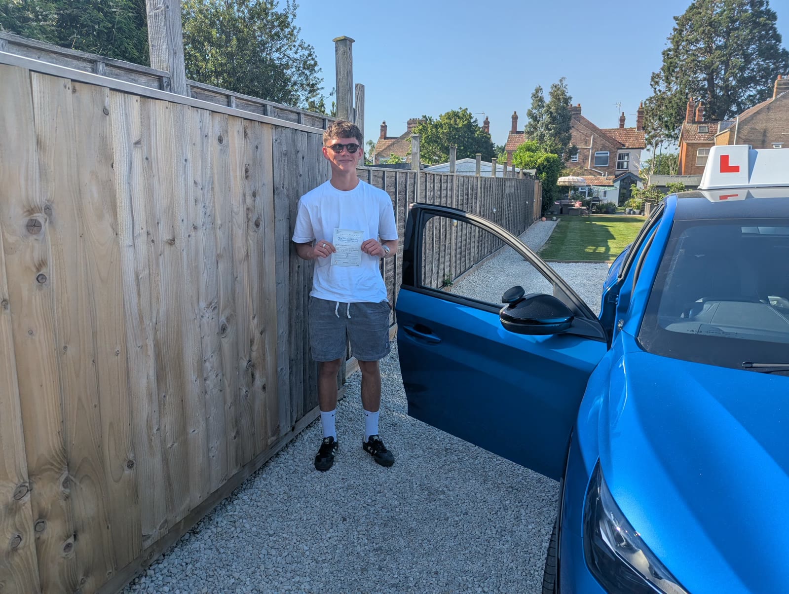 A learner holds their pass certificate beside the open car door