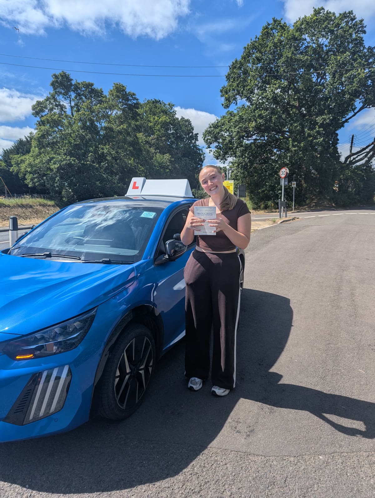 A learner celebrates passing beside the metallic blue Peugeot