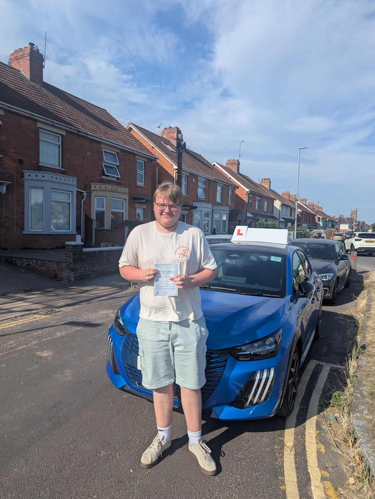 A learner celebrates passing their driving test with the tuition car behind them